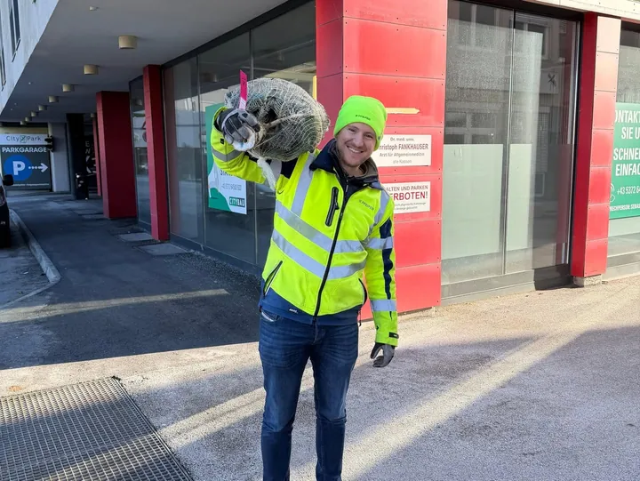 Ein Helfer trägt einen verpackten Christbaum zur Lieferung